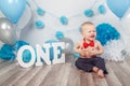 Caucasian baby boy in dark pants and blue bow tie celebrating his first birthday with letters one and balloons Royalty Free Stock Photo