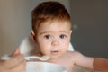 Caucasian baby boy with messy face eating porridge on a high chair. Adorable baby eating food. His mother feeds him with Royalty Free Stock Photo