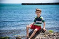 Caucasian baby boy is sitting at the beach. Cute child is playing with roks and shellfishes muscle-fish on the sand in summer day