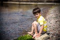 Caucasian baby boy is sitting at the beach. Cute child is playing with roks and shellfishes muscle-fish on the sand in summer day