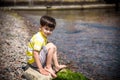 Caucasian baby boy is sitting at the beach. Cute child is playing with roks and shellfishes muscle-fish on the sand in summer day