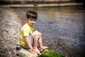 Caucasian baby boy is sitting at the beach. Cute child is playing with roks and shellfishes muscle-fish on the sand in summer day