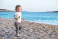 Caucasian baby girl with blond curly hair looking at camera on sandy beach near blue sea.Happy,pretty,adorable,cute Royalty Free Stock Photo