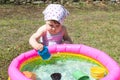 Caucasian baby girl playing toys close to inflatable pool full of water, meadow on backyard Royalty Free Stock Photo