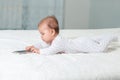 A caucasian baby in sliders is lying on the bed and playing with a smartphone. Side view. Concept of children& x27;s games Royalty Free Stock Photo