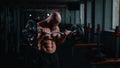 Caucasian bald topless man doing an exercise with a barbell in the gym. Bicep curls with weights.