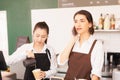 Caucasian barista woman confirms online orders with customer via mobile, Asian barista woman fills white milk into takeaway coffee