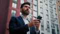 Caucasian bearded man entrepreneur businessman hold cellphone texting messages stand in city with modern office Royalty Free Stock Photo