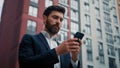 Caucasian bearded man entrepreneur businessman hold cellphone texting messages stand in city with modern office Royalty Free Stock Photo