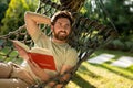 Caucasian bearded young man lying in hammock with a book in hands Royalty Free Stock Photo