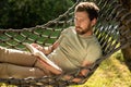 Caucasian bearded young man lying in hammock with a book in hands Royalty Free Stock Photo