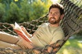 Caucasian bearded young man lying in hammock with a book in hands Royalty Free Stock Photo