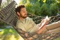 Caucasian bearded young man lying in hammock with a book in hands Royalty Free Stock Photo