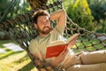 Caucasian bearded young man lying in hammock with a book in hands Royalty Free Stock Photo