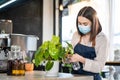 Caucasian beautiful Coffee shop owner wear protective mask due to Covid-19 pandemic, spraying water on green leaf inside coffeehou