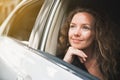 Caucasian beautiful female with a little smile sitting inside the car and looking outside car window. Automobile rental. Royalty Free Stock Photo