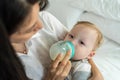 Caucasian beautiful mother holding and feeding baby from milk bottle. Attractive loving family, mom sit on bed and carry sleepy Royalty Free Stock Photo