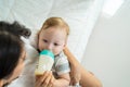 Caucasian beautiful mother holding and feeding baby from milk bottle. Attractive loving family, mom sit on bed and carry sleepy Royalty Free Stock Photo