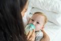 Caucasian beautiful mother holding and feeding baby from milk bottle. Attractive loving family, mom sit on bed and carry sleepy Royalty Free Stock Photo