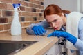 Caucasian beautiful red-headed female in casual clothes wearing rubber glove and holding chemica spray in kitchen