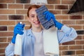 Caucasian beautiful red-headed female in casual clothes wearing rubber glove and holding chemica spray in kitchen