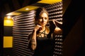 Caucasian beautiful tattooed girl, rock singer recording the sound in professional studio with mic on the striped wall