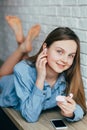 Caucasian beautiful teenage girl in blue shirt with blue eyes crossed her legs looking at the camera and smiling, puts on headphon Royalty Free Stock Photo