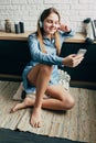 Caucasian beautiful teenager in blue shirt sits on the floor in apartments with beautiful loft interior and looks into the phone l