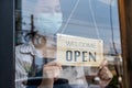 Caucasian beautiful waitress wear mask, turns open sign on glass door. Attractive Coffee shop owner prepare to welcome customer to Royalty Free Stock Photo