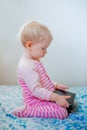 Caucasian blond baby girl sitting in bed playing with digital tablet with funny face expression Royalty Free Stock Photo