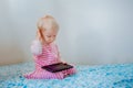 Caucasian blond baby girl sitting in bed playing with digital tablet with funny face expression Royalty Free Stock Photo