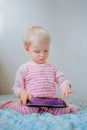 Caucasian blond baby girl sitting in bed playing with digital tablet with funny face expression Royalty Free Stock Photo