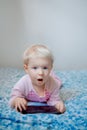 Caucasian blond baby girl sitting in bed playing with digital tablet with funny face expression Royalty Free Stock Photo