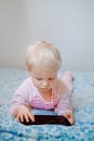 Caucasian blond baby girl sitting in bed playing with digital tablet with funny face expression Royalty Free Stock Photo