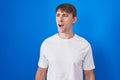 Caucasian blond man standing over blue background angry and mad screaming frustrated and furious, shouting with anger Royalty Free Stock Photo