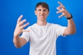 Caucasian blond man standing over blue background shouting frustrated with rage, hands trying to strangle, yelling mad Royalty Free Stock Photo