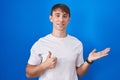 Caucasian blond man standing over blue background showing palm hand and doing ok gesture with thumbs up, smiling happy and Royalty Free Stock Photo