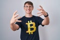 Caucasian blond man wearing bitcoin t shirt shouting frustrated with rage, hands trying to strangle, yelling mad Royalty Free Stock Photo