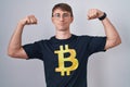 Caucasian blond man wearing bitcoin t shirt showing arms muscles smiling proud
