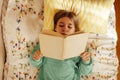 Caucasian blond teenage girl is lying on the bed and reading book