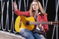 Caucasian Blond woman Posing in Red Leather Jacket and Jeans with Guitar Outdors on Dark Street