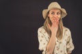 Caucasian blond woman wearing wide sun hat and polka-dot shirt covering mouth with hand looking to the right. Silly Royalty Free Stock Photo