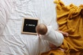 Caucasian blonde baby eight months old lying on cozy bed with yellow knitted blanket at home. Kid wearing white clothing Royalty Free Stock Photo