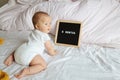 Caucasian blonde baby eight months old lying on cozy bed with yellow knitted blanket at home. Kid wearing white clothing Royalty Free Stock Photo