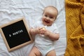 Caucasian blonde baby eight months old lying on cozy bed with yellow knitted blanket at home. Kid wearing white clothing Royalty Free Stock Photo