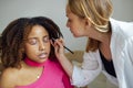 Caucasian blonde female master makes makeup for her dark skinned client in a beauty salon