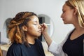 Caucasian blonde female master makes makeup for her dark skinned client in a beauty salon