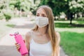 Caucasian blonde sports girl wearing face mask walking in the park and holding a bottle of water Royalty Free Stock Photo