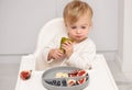 Caucasian blonde toddler eating from silicone plate fresh pear,fruits,berries,having meal on white background.Kid self