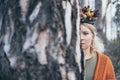 Caucasian blonde woman with atumn leaves wreath stands behind the tree trunk as foreground Royalty Free Stock Photo